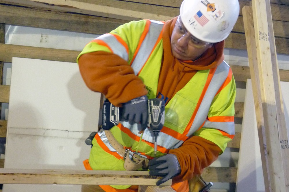 A construction worker drills a 2x4 into a beam.