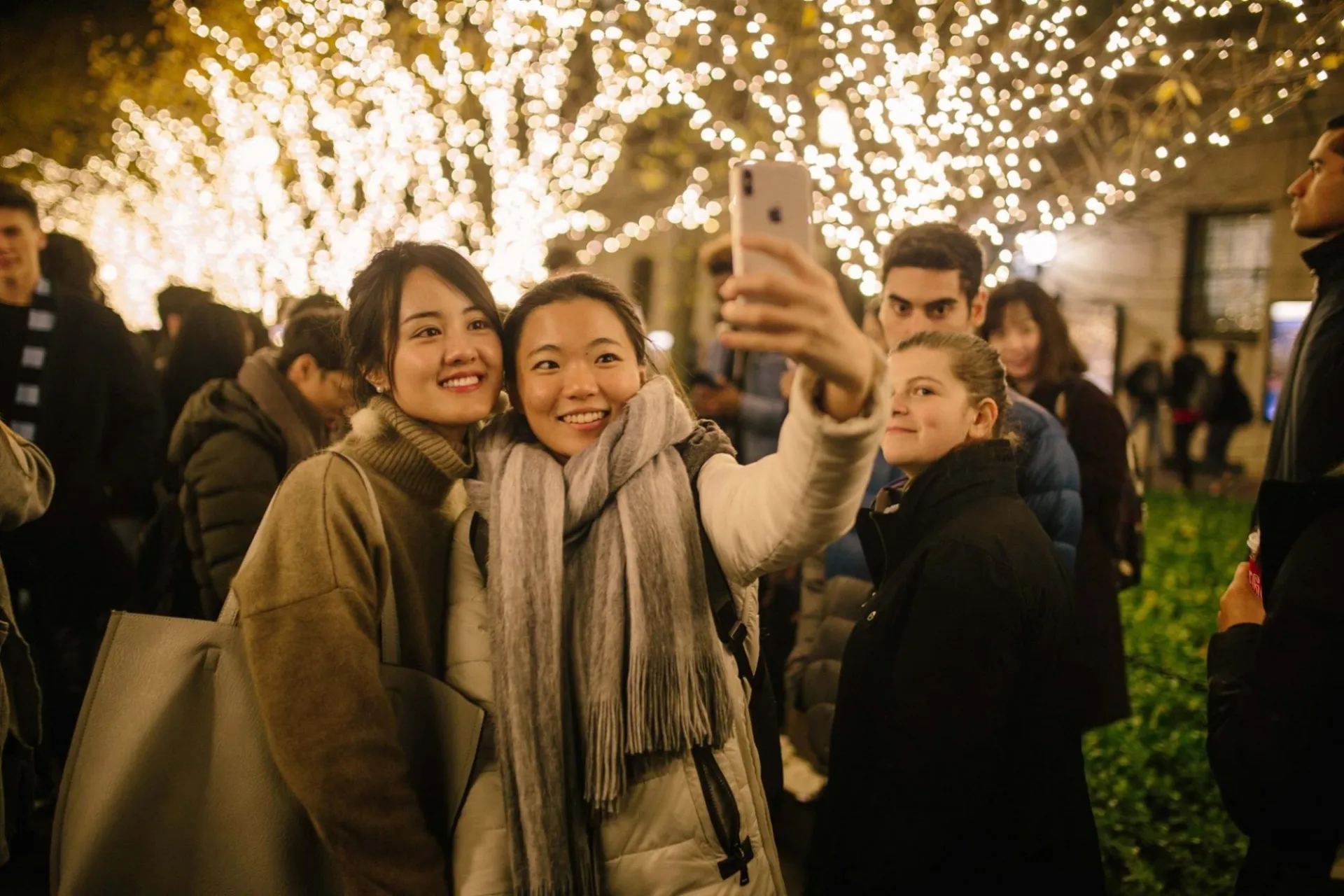 Students take photo in front of lit trees on College Walk