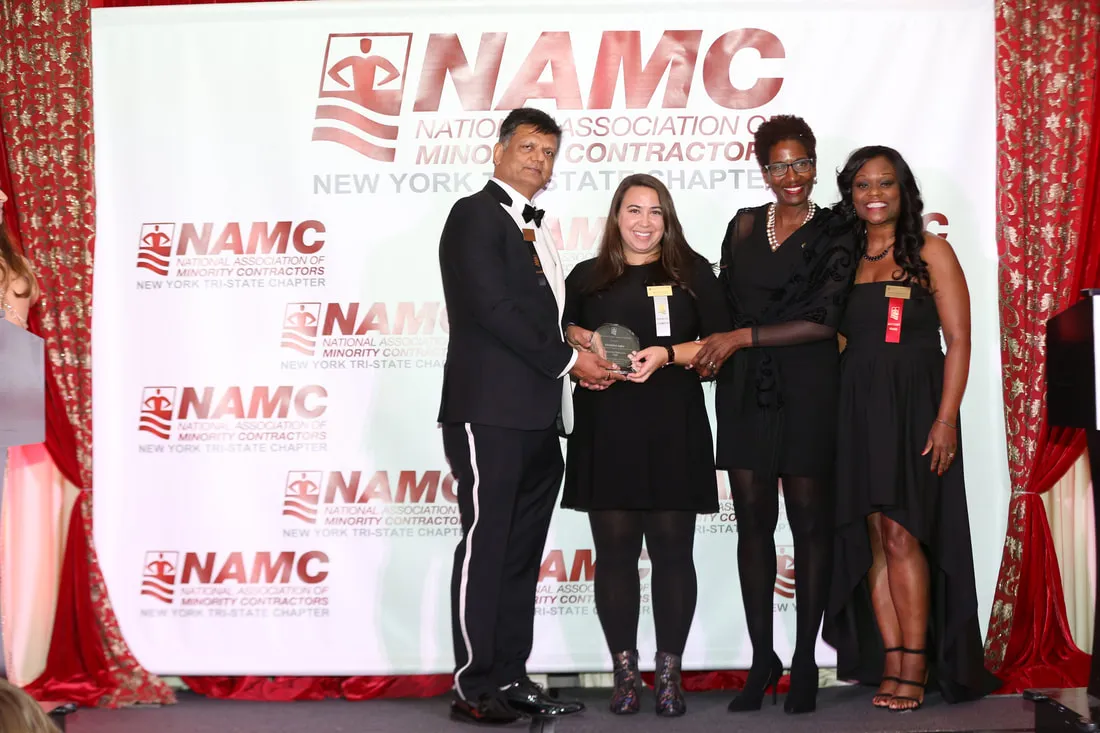 Christine Salto receiving the Diversity Champion award from three people in front of a white screen that has a red National Association of Minority Contractors logo on it. 