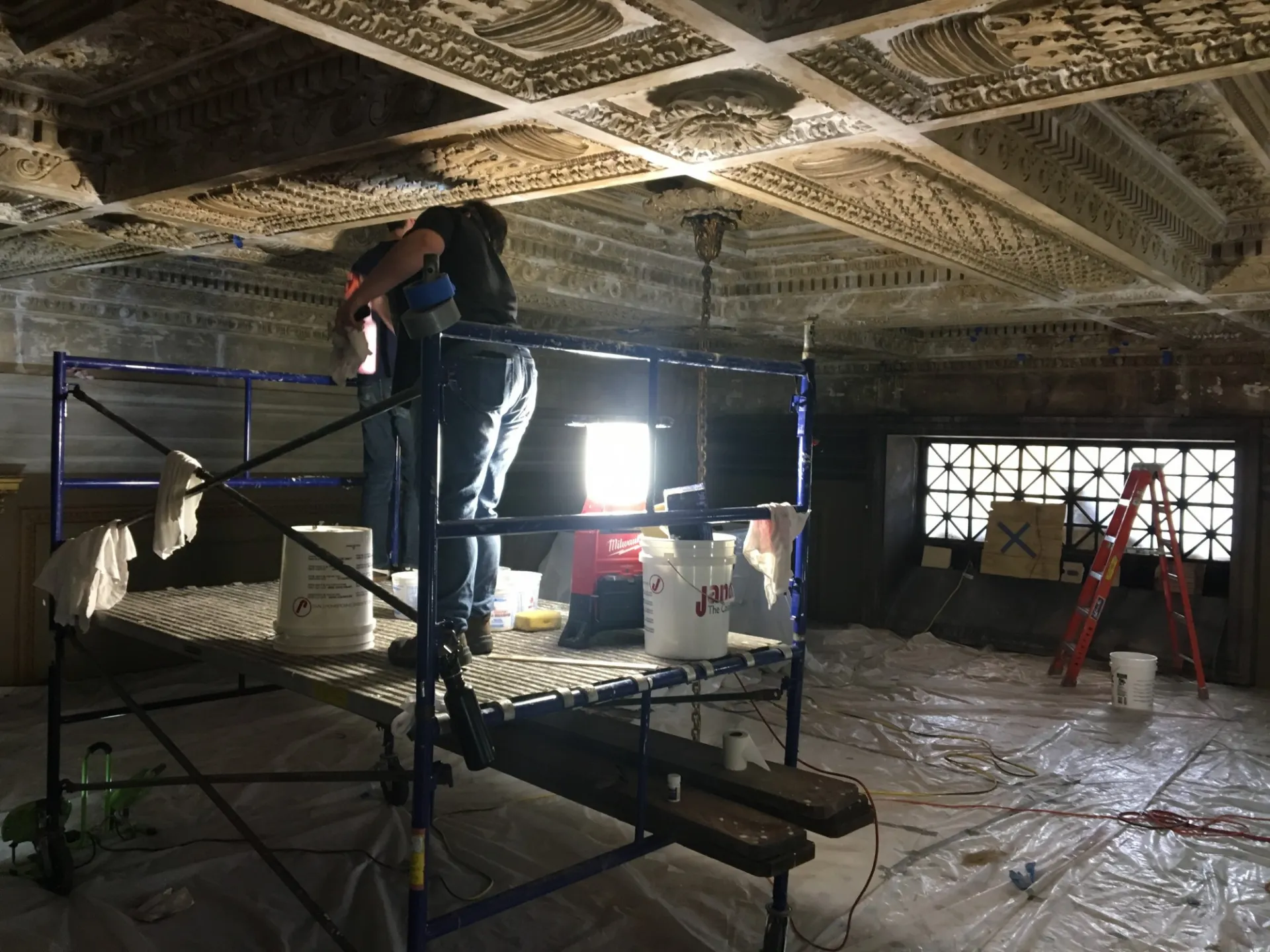 Conservators at work making repairs to the plaster ceiling. Site protection includes elaborate sound barriers with felt-tip panels, padding lining the walls., and plastic covering, collectively designed to minimize noise and protect from dust.
