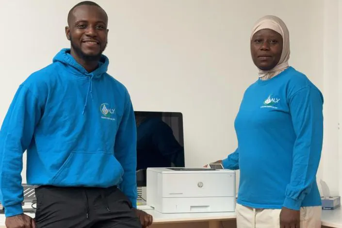 Two people stand next to a new HP printer in their office.