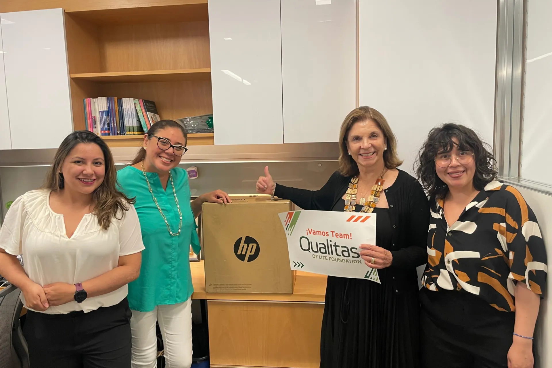 A group of people gather around a boxed HP printer and hold a sign that says, "Vamos Team - Qualitas for Life Foundation"
