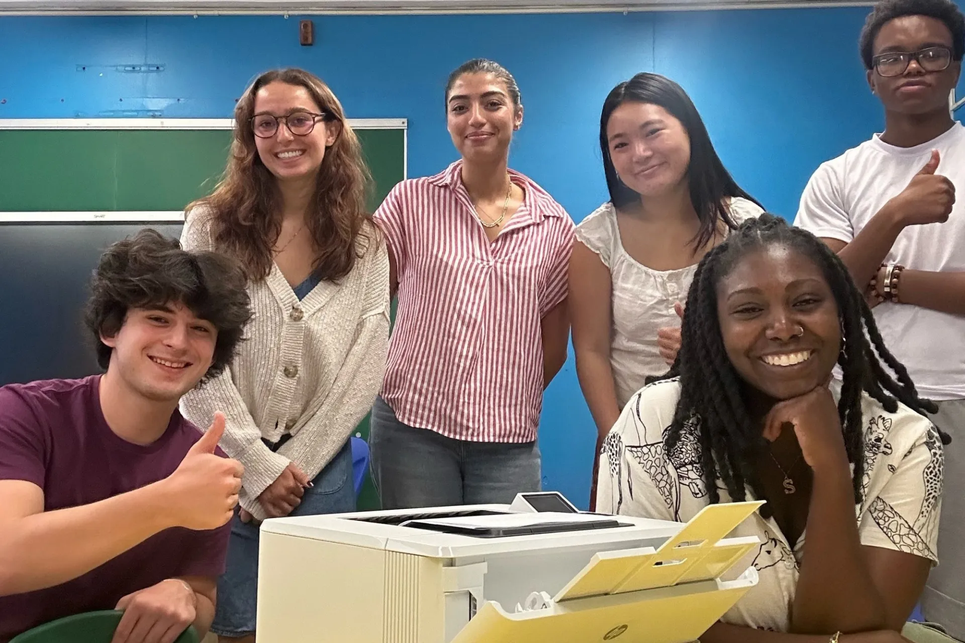 A group of young adults pose next to a new HP printer in a room.