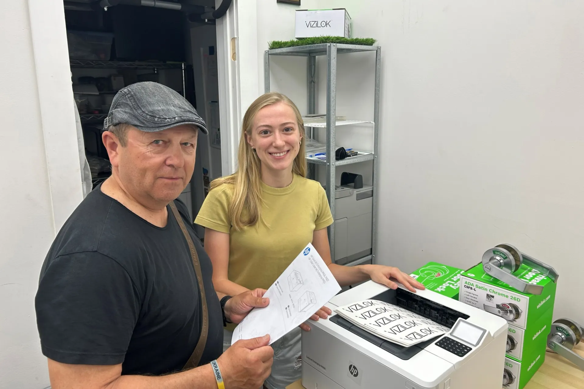 Two people gather in front of a new printer that has printed mew company logos. 