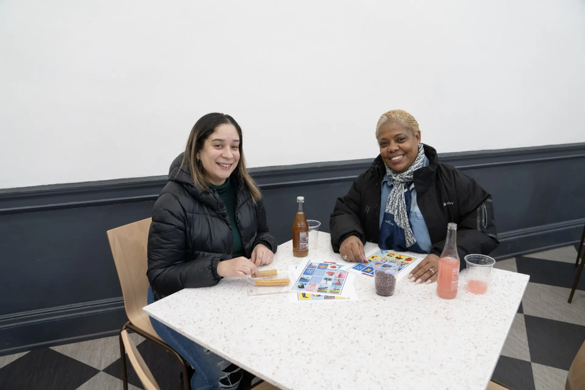 Two CUFO staff members sitting at a table together with Loteria game boards, Jarritos soda, and churros.