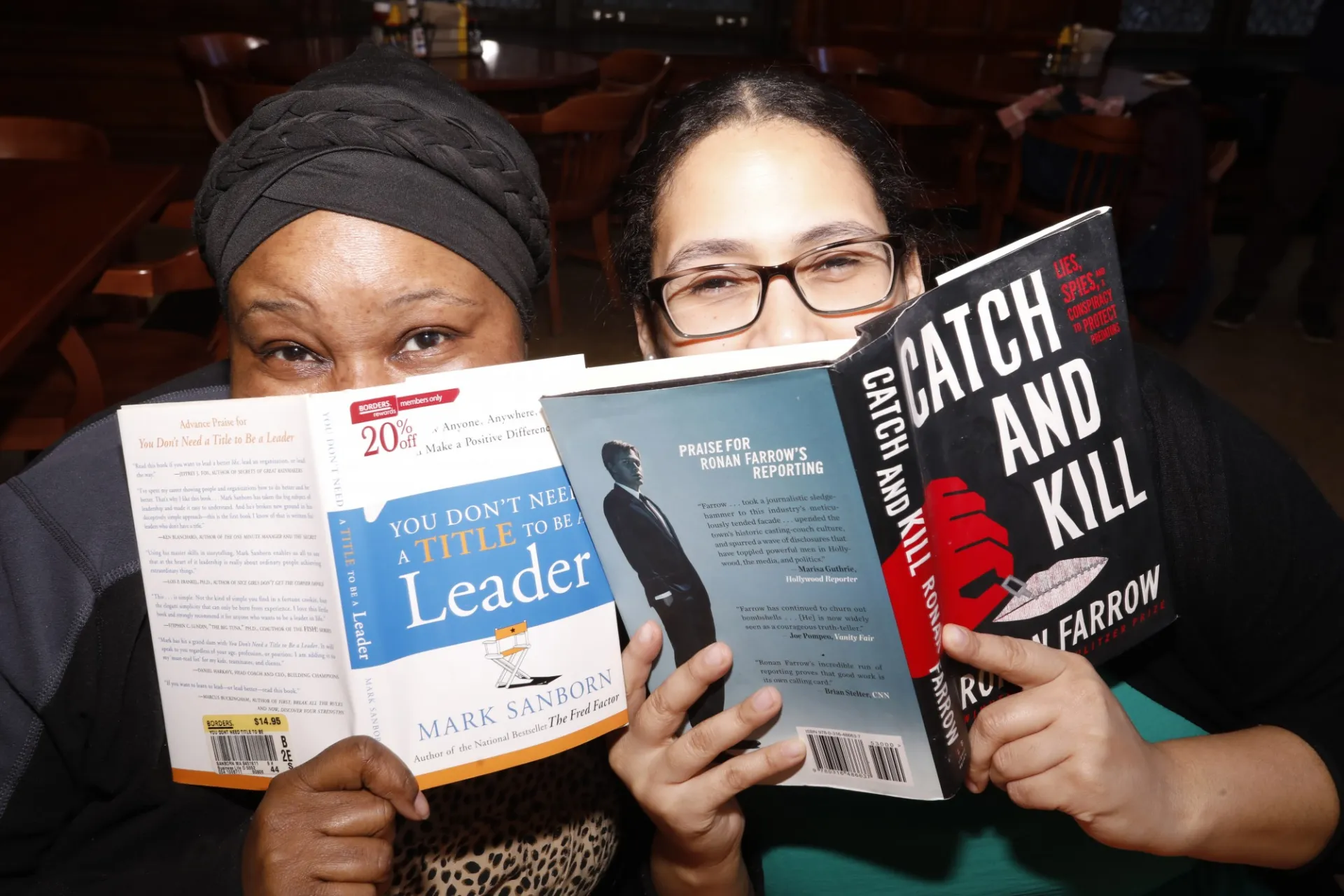 Two people hold books in front of their faces so only their eyes are visible.