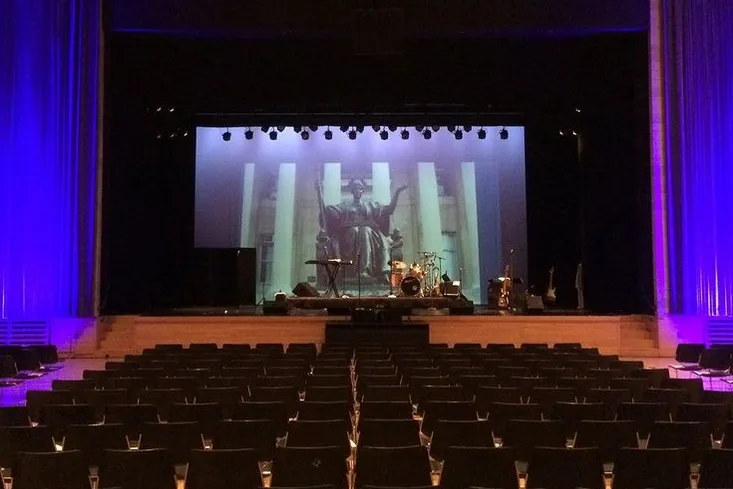 An auditorium is lit up with purple lights, with an image of Columbia's Alma Mater projected on the screen on stage
