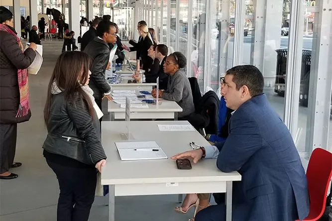 People walk up to tables and speak to hiring managers about job openings.