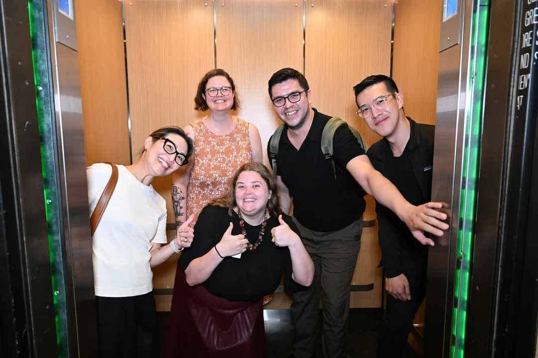 Five people stand in the new IAB elevators and smile as they prepare to take a ride up.