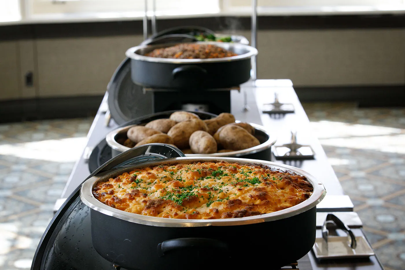 A view of the serving bar showing mac and cheese, baked potatoes, quinoa pilaf, and vegetable medley. 