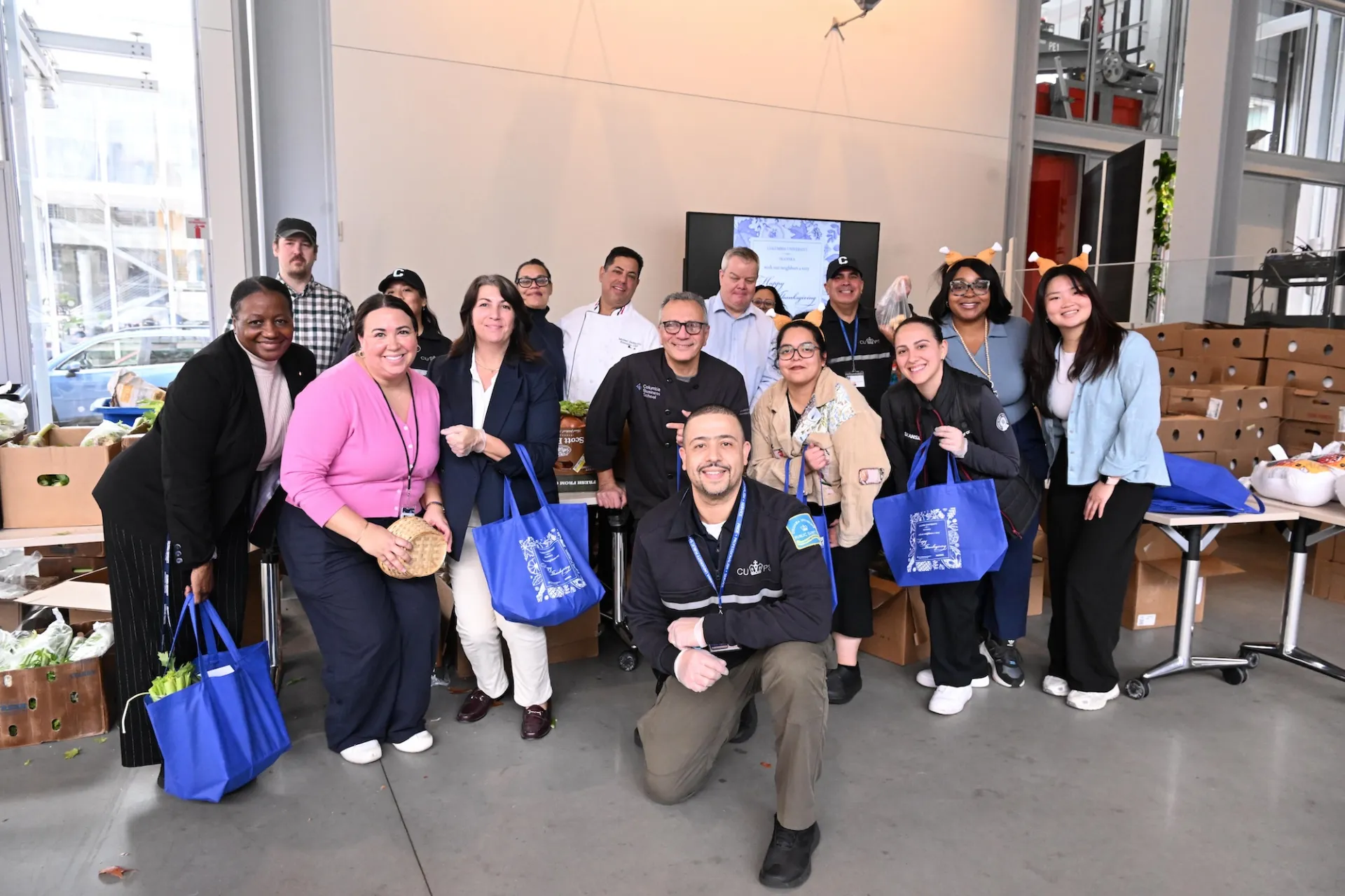 Staff of Columbia and Skanska stand together holding tote bags full of food and with boxes of vegetables behind them.