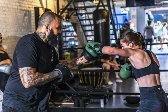 Two people spar inside of a boxing gym.