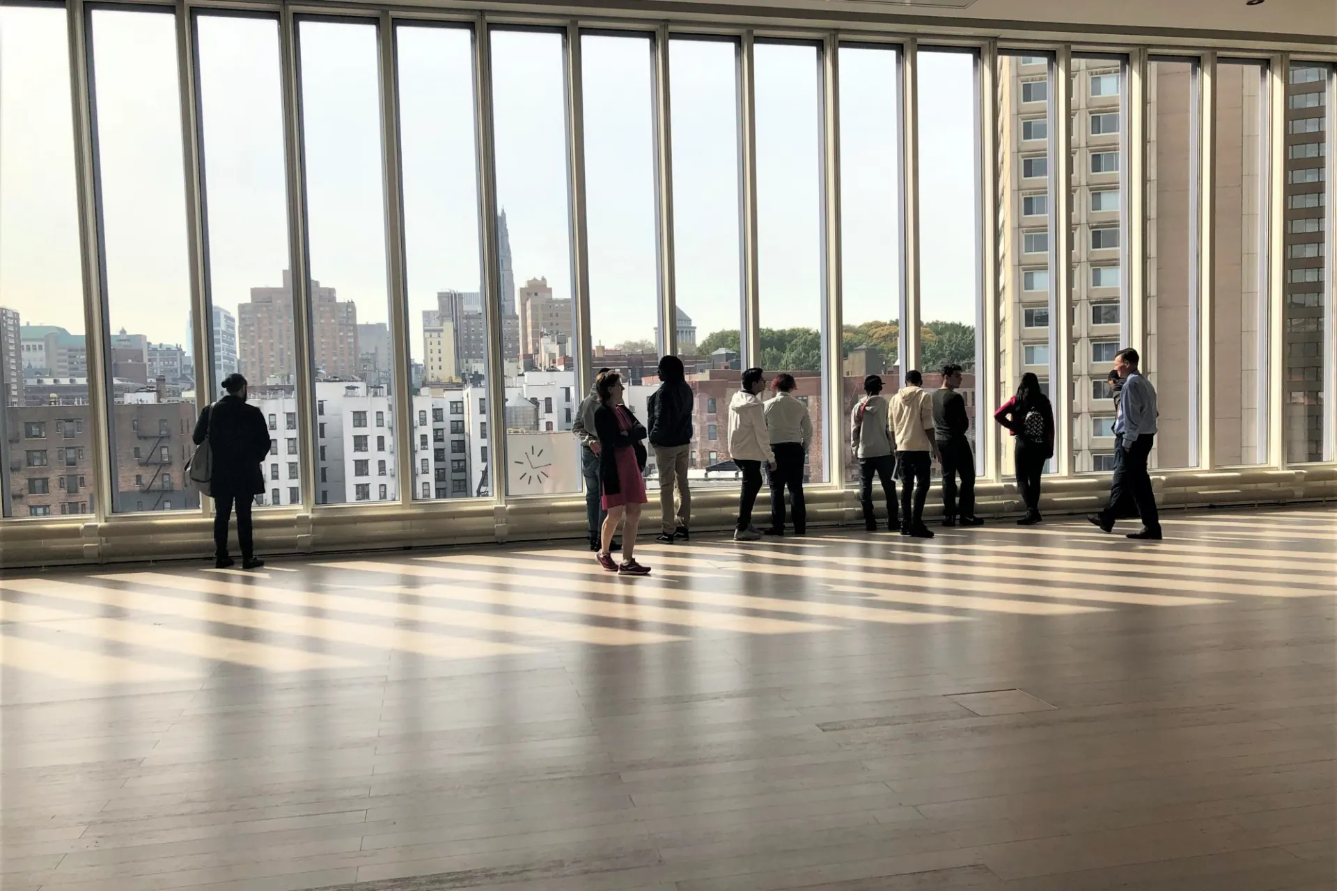 A group of students look out very large windows onto the Manhattanville campus construction site.