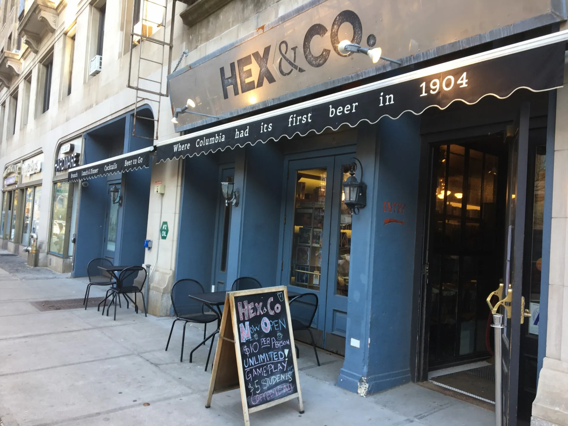 The storefront of Hex & Co which has a rolled up canopy that says "Where Columbia had its first beer in 1904 and some tables and chairs outside the entrance.
