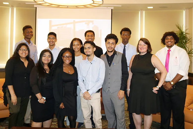 A group of high school interns stand together with a Facilities and Operations employee in front of a projection screen.