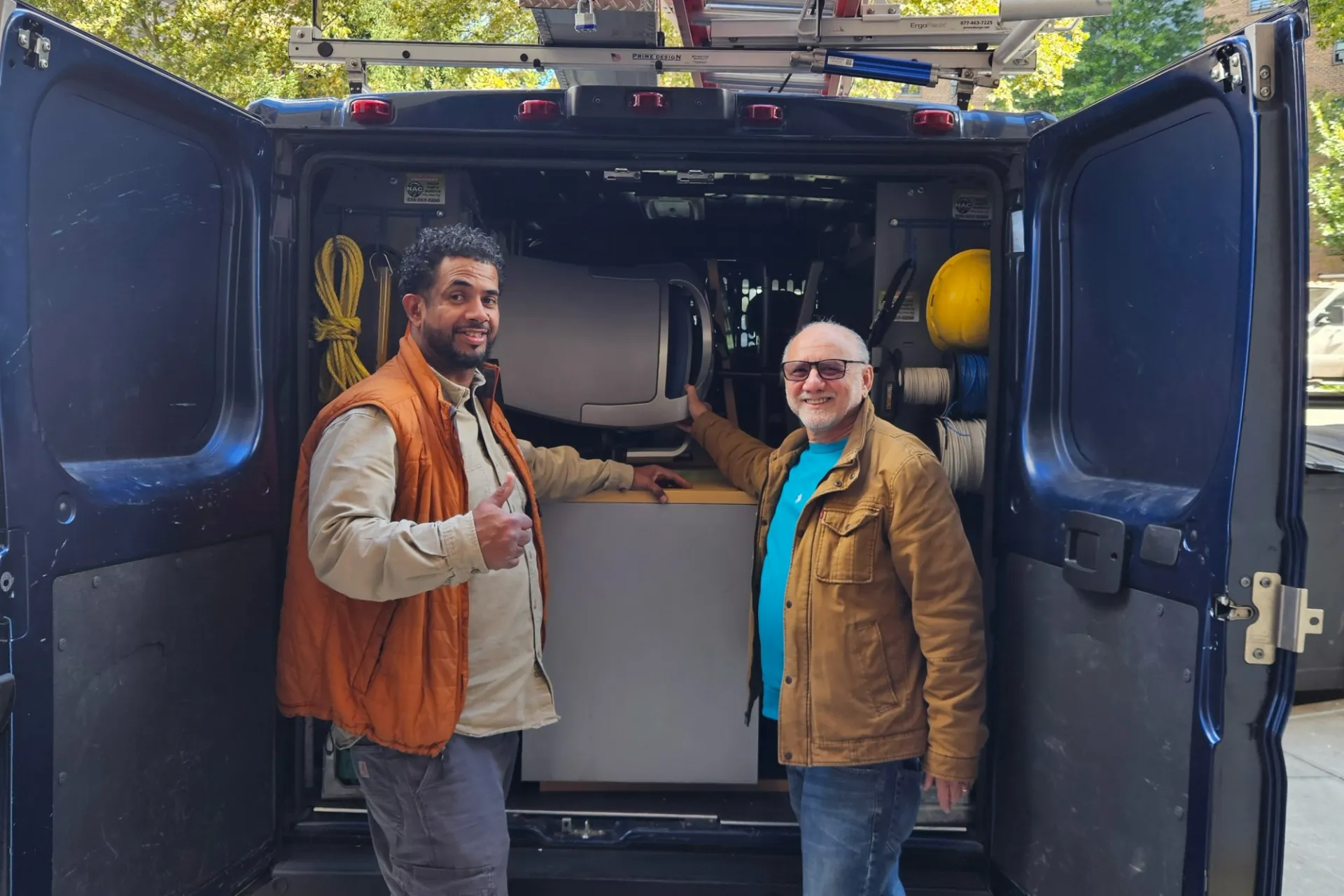 Two people stand at the end of an open utility van that has furniture packed inside and smiled.