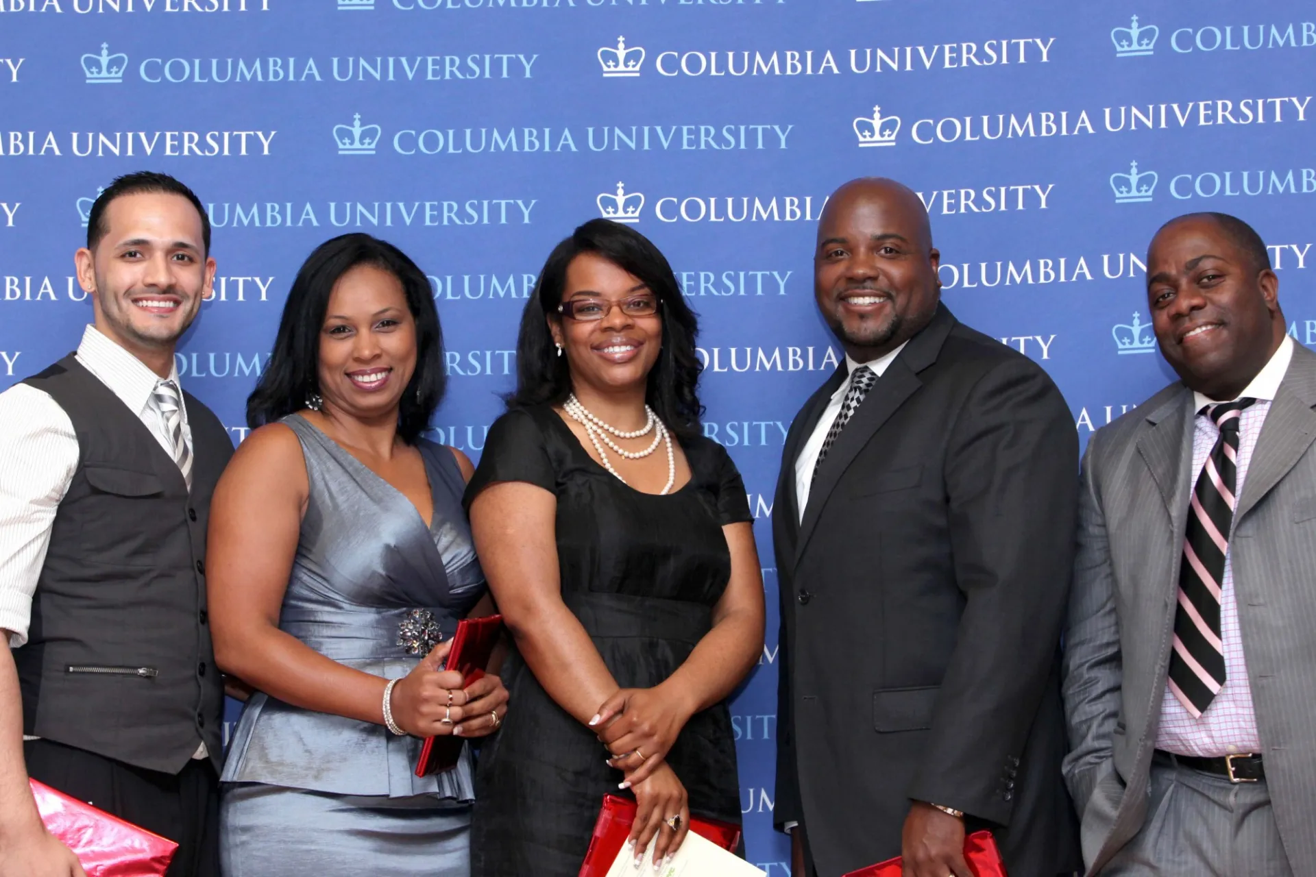 A group of people stand together with a blue Columbia University backdrop behind them