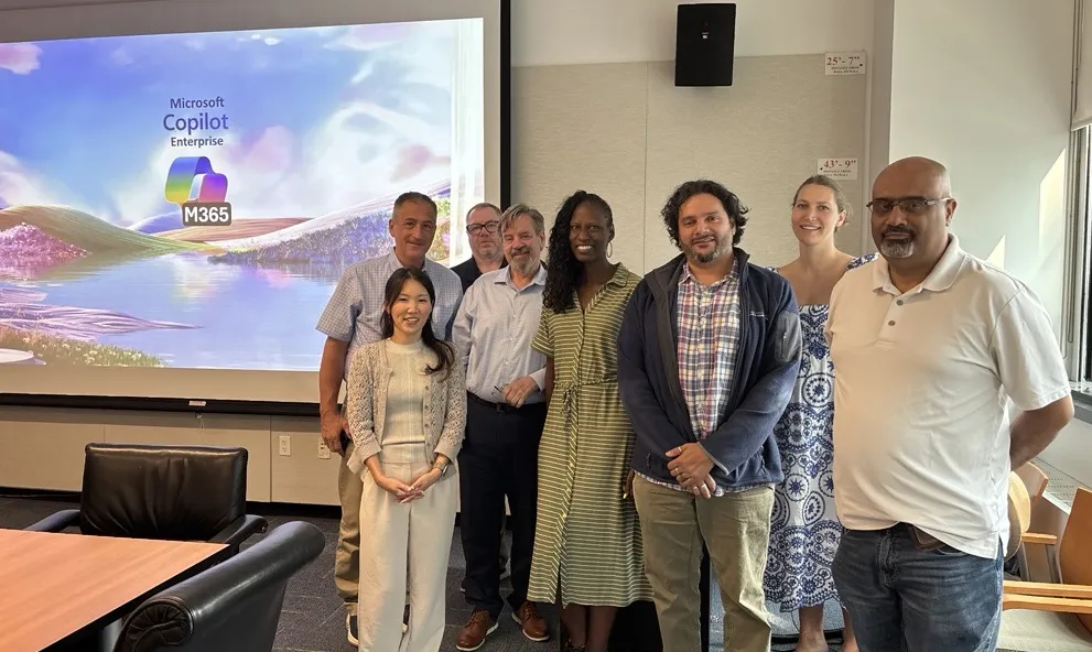 8 people stand in Studebaker conference room at Columbia's Manhattanville campus in front of a powerpoint that has the Microsoft Copilot 365 logo.