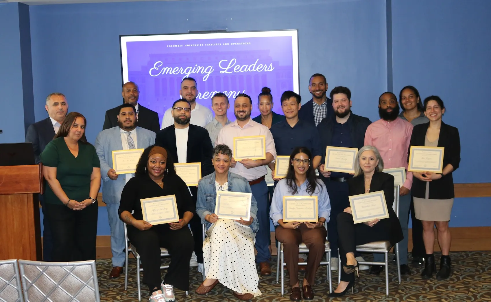 group of staff holding framed certificates in front of sign that says Emerging Leaders