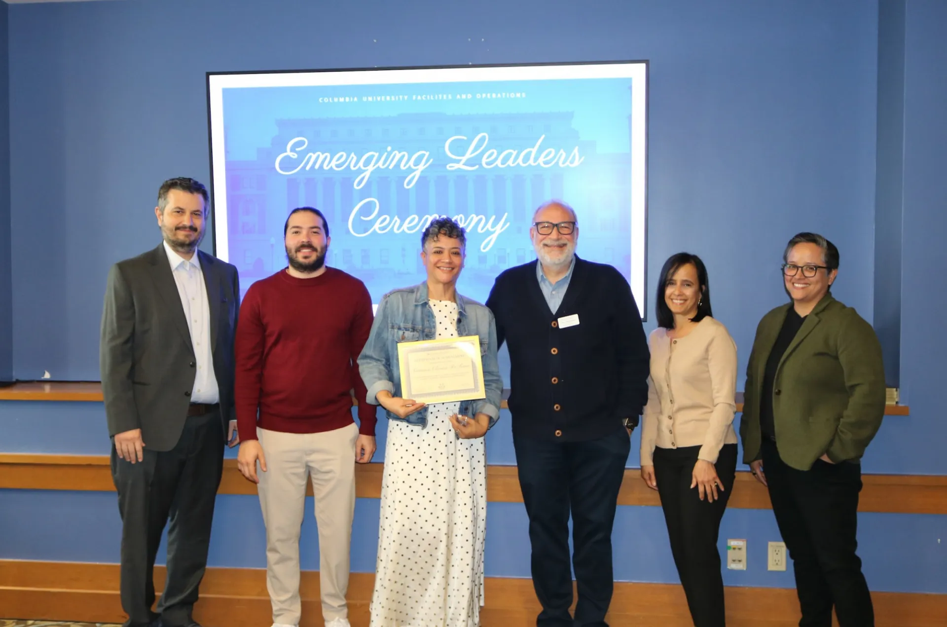 Six people stand in front of Emerging Leaders Ceremony Sign. One holds a certificate