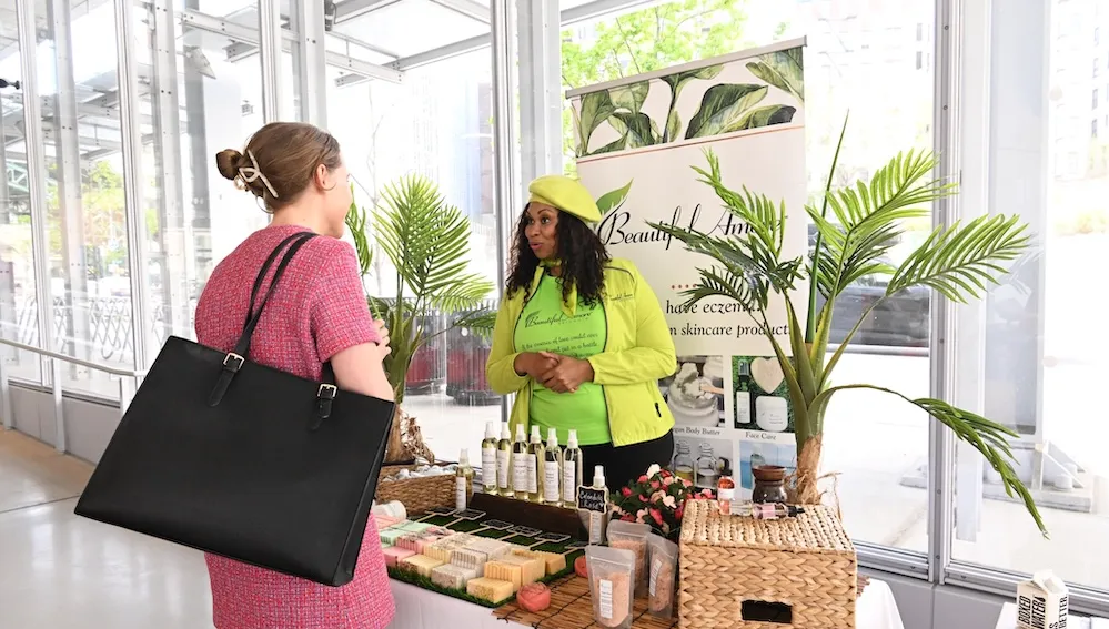 Two women at a skincare booth with products and a 'Beautiful Amore Skincare' banner.