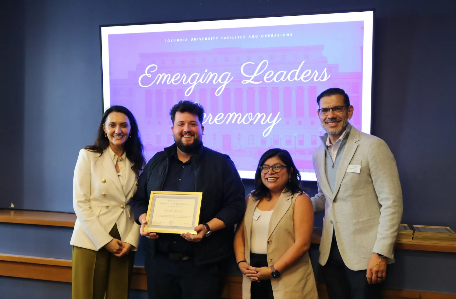 Four staff members in front of a sign that says "Emerging Leaders Ceremony." One holds a certificate.