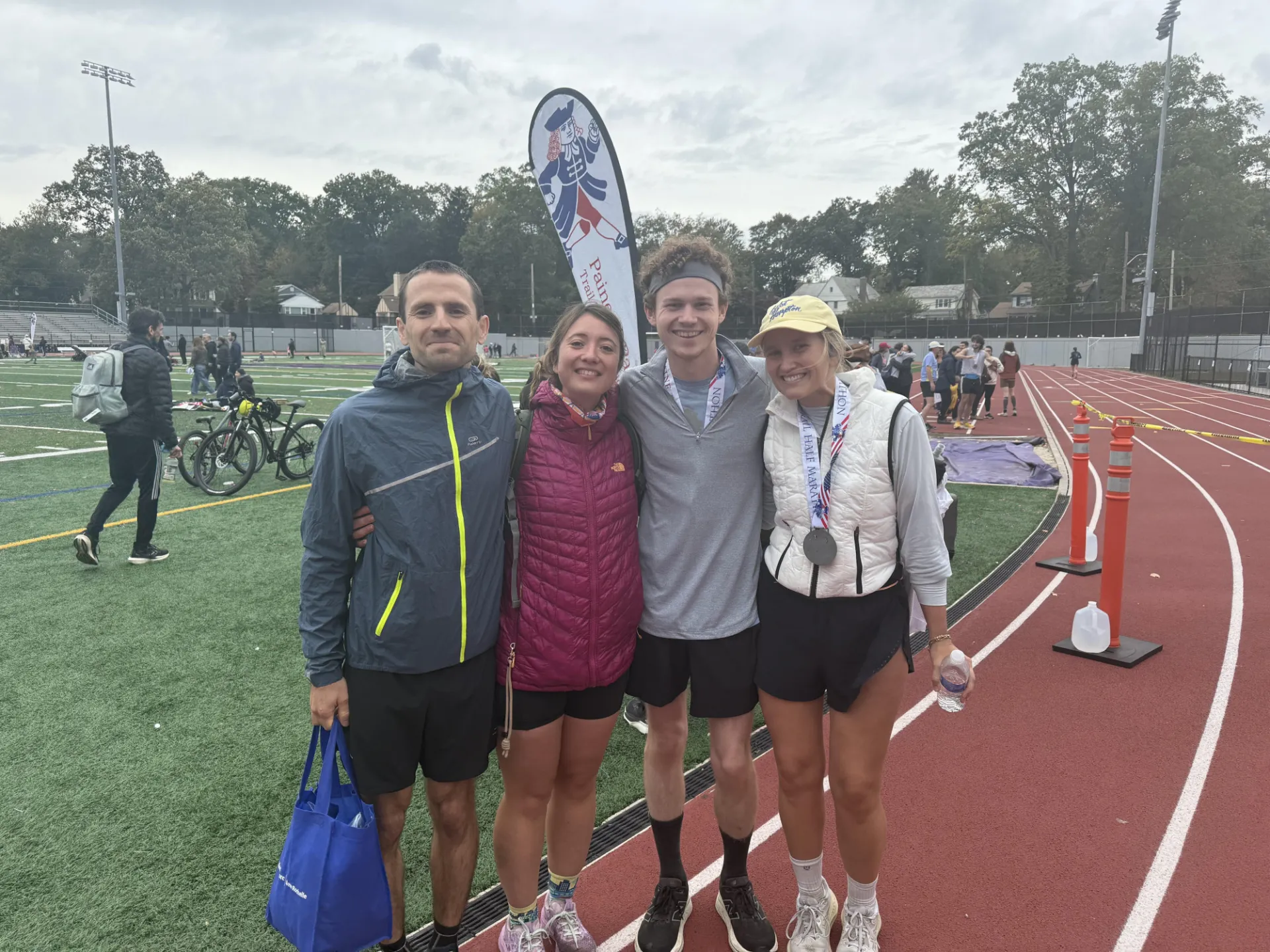 Four people stand together on an outdoor track wearing medals that say Half Marathon.
