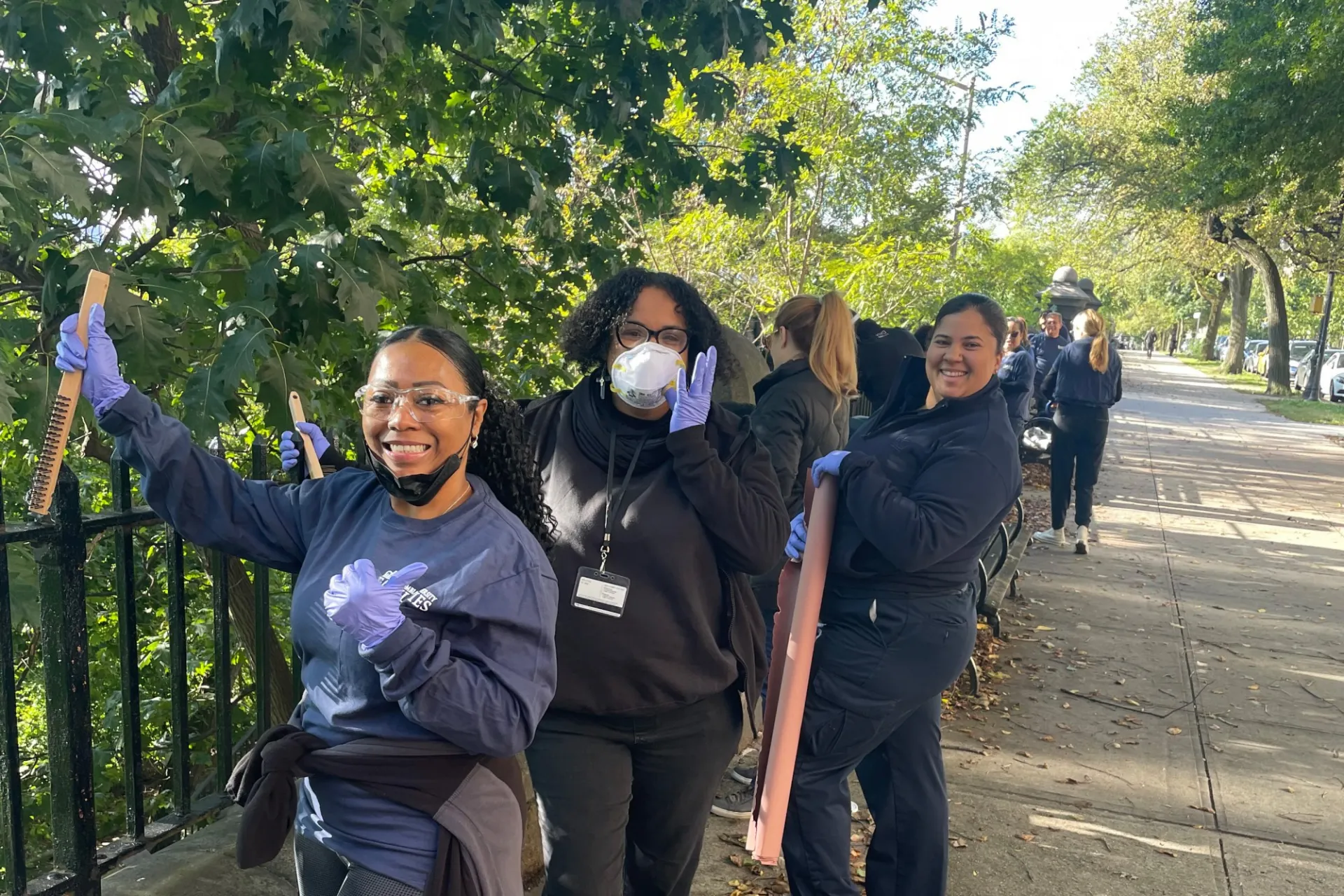 Columbia Residential employees pose at a railing alongside Morningside Drive with tools to scrape old paint off.