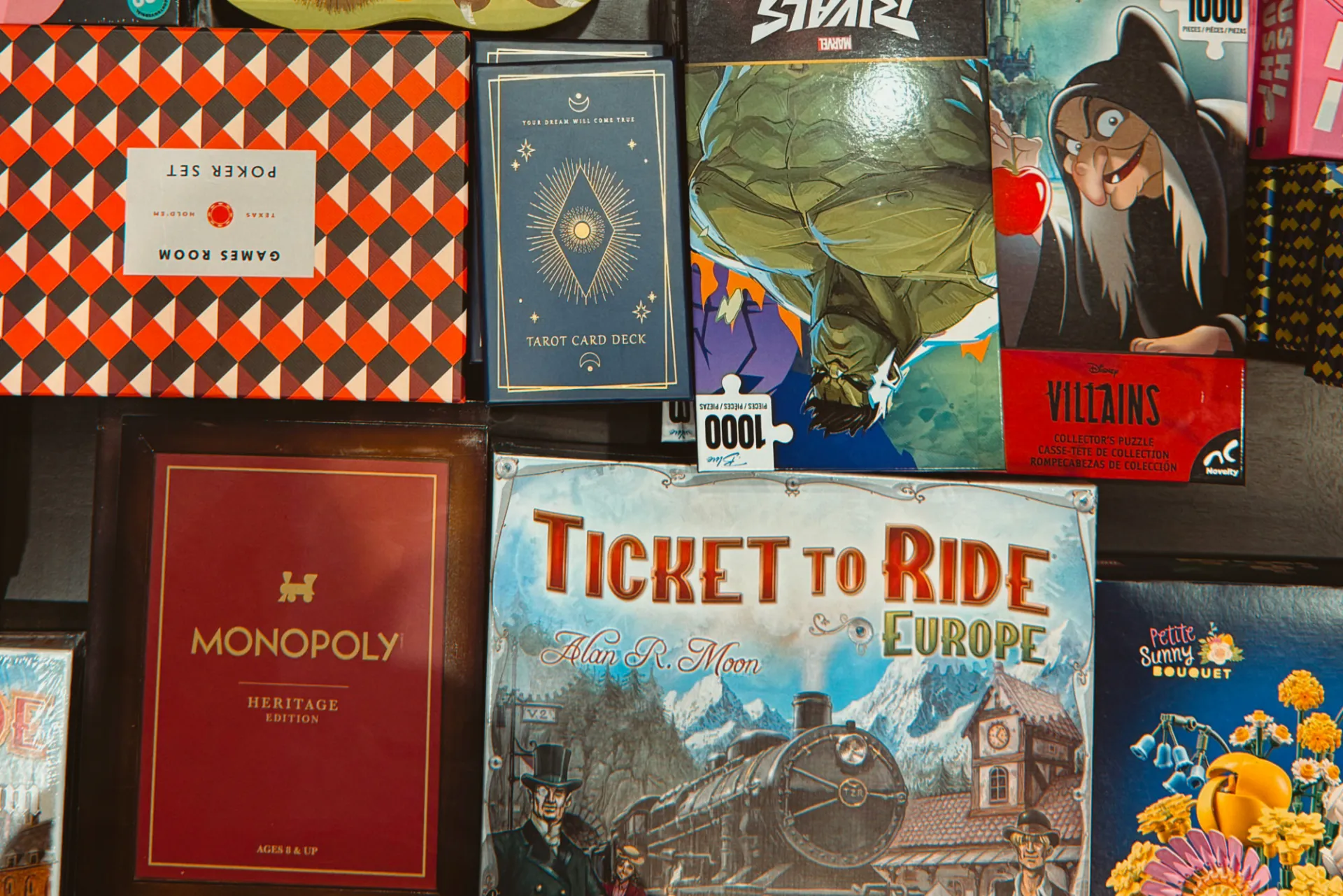 A selection of different board games, puzzles, and tarot cards, including a poker set, Ticket to Ride Europe, Monopoly, and Disney Villains and Marvel Rivals puzzles.