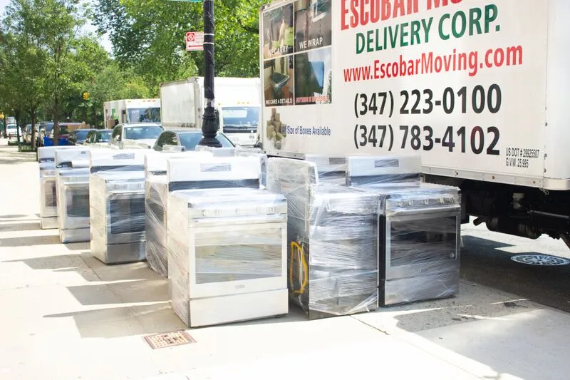 Stoves wrapped in plastic sit on a sidewalk next to a moving truck