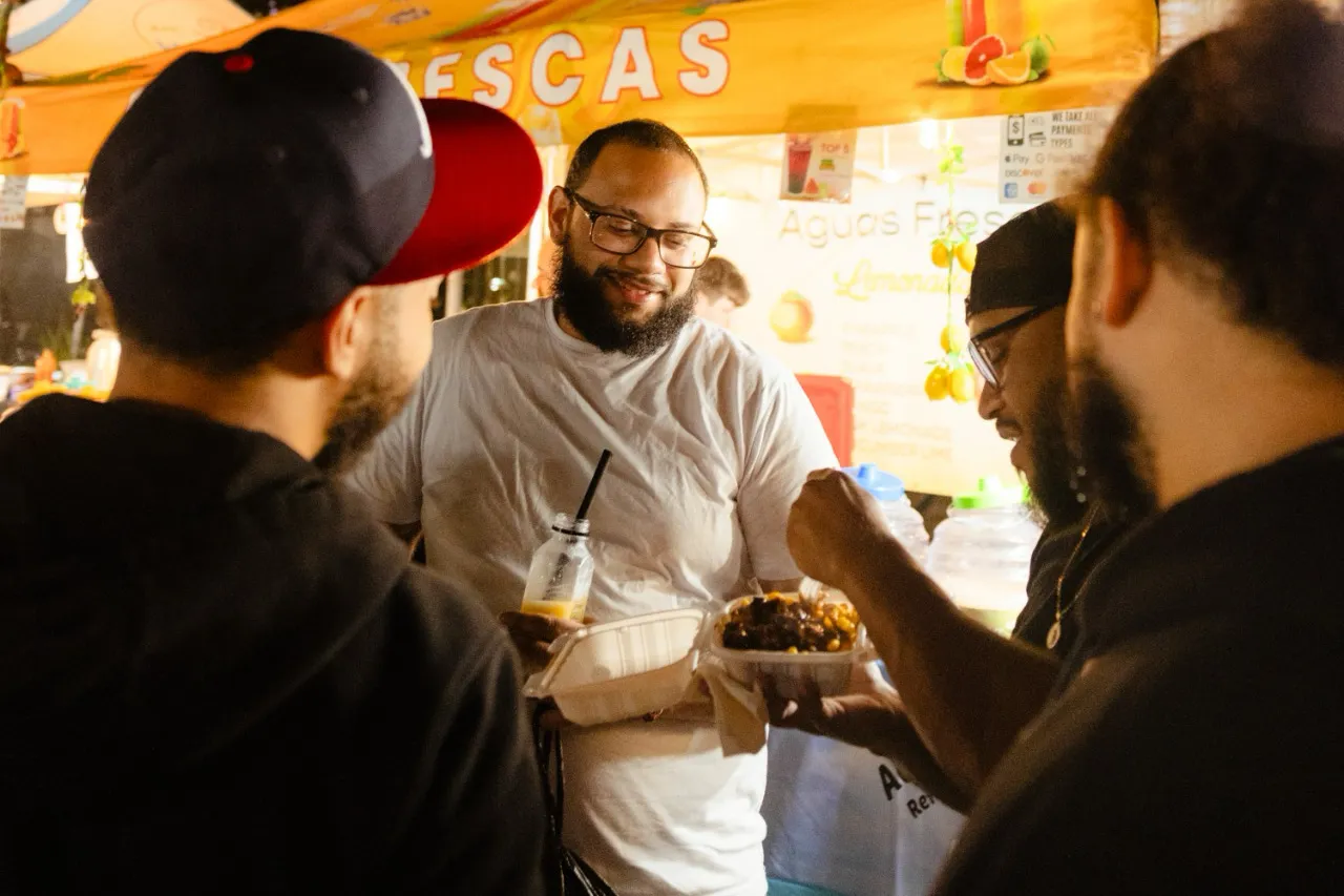 People gather around a plate of food purchased from a vendor at the Uptown Night Market.