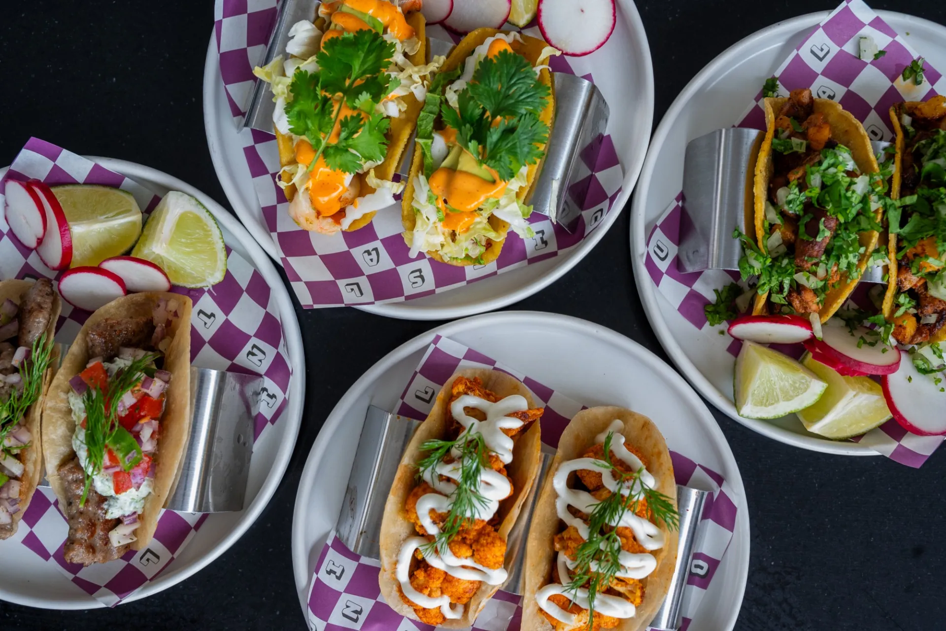 An overhead shot of four plates with two tacos each on them, with radish and lime included on each plate as garnishes