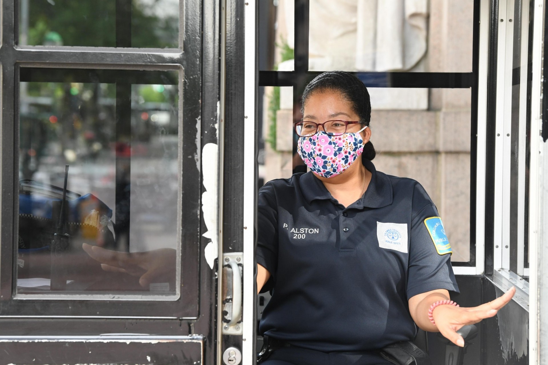 Female Public Safety Officer with glasses and a facemask on inside of a guard booth 