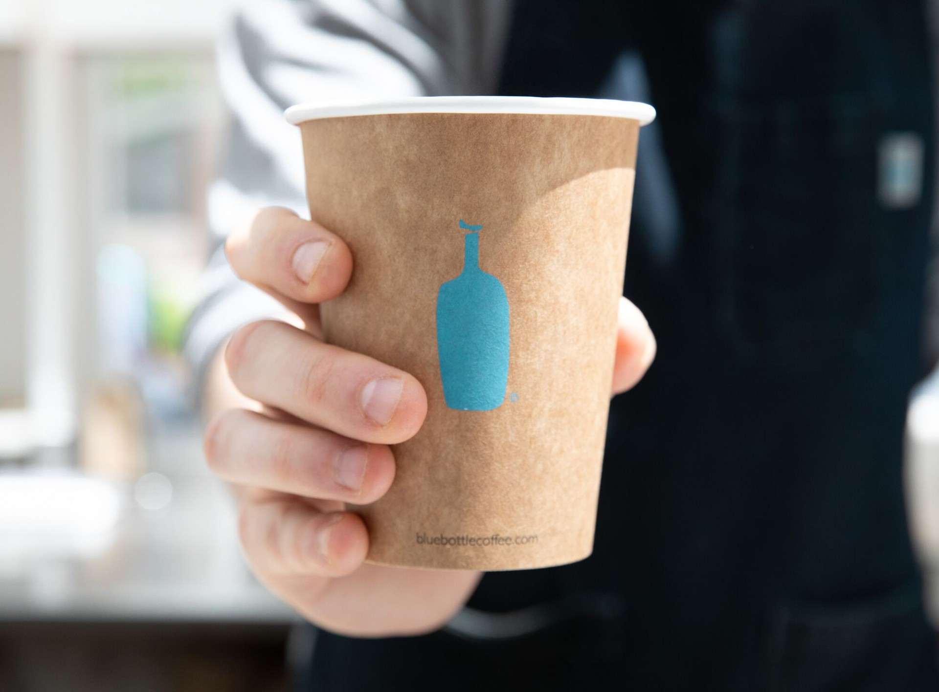 A hand holding a Blue Bottle Coffee