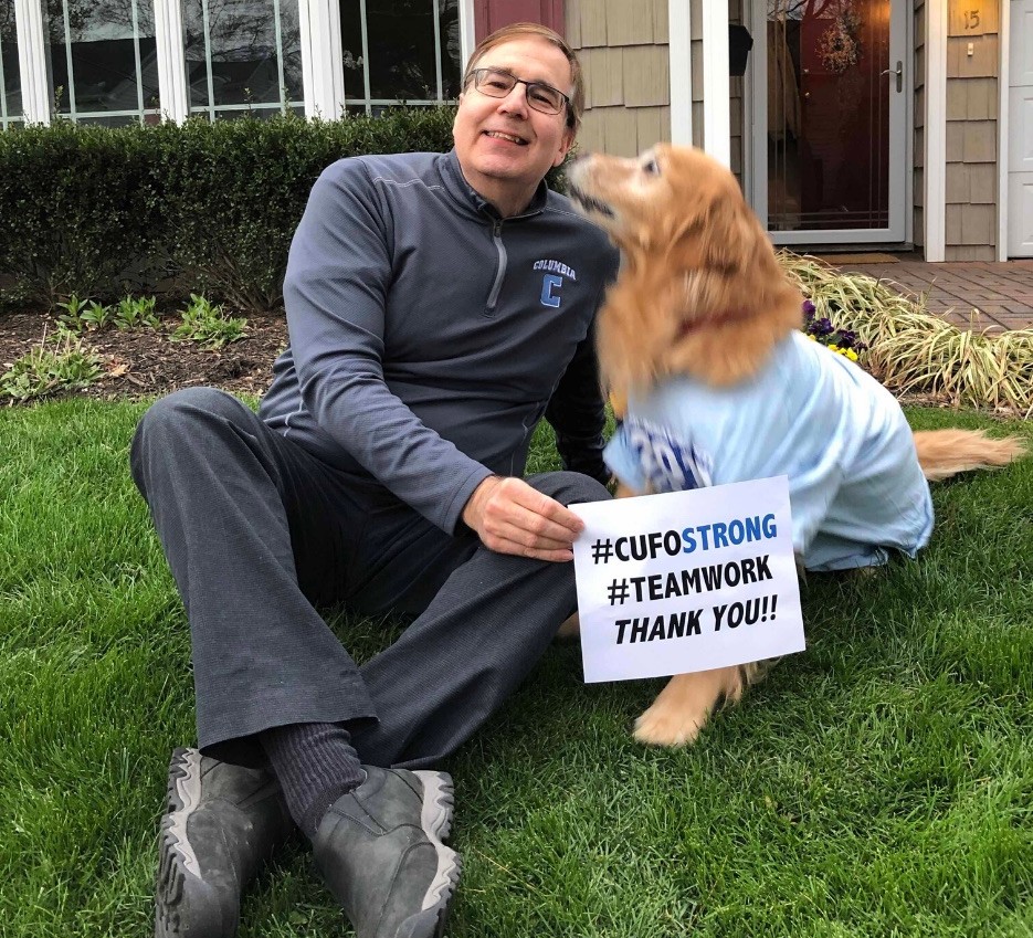 man sits with dog on grass holding thank you sign