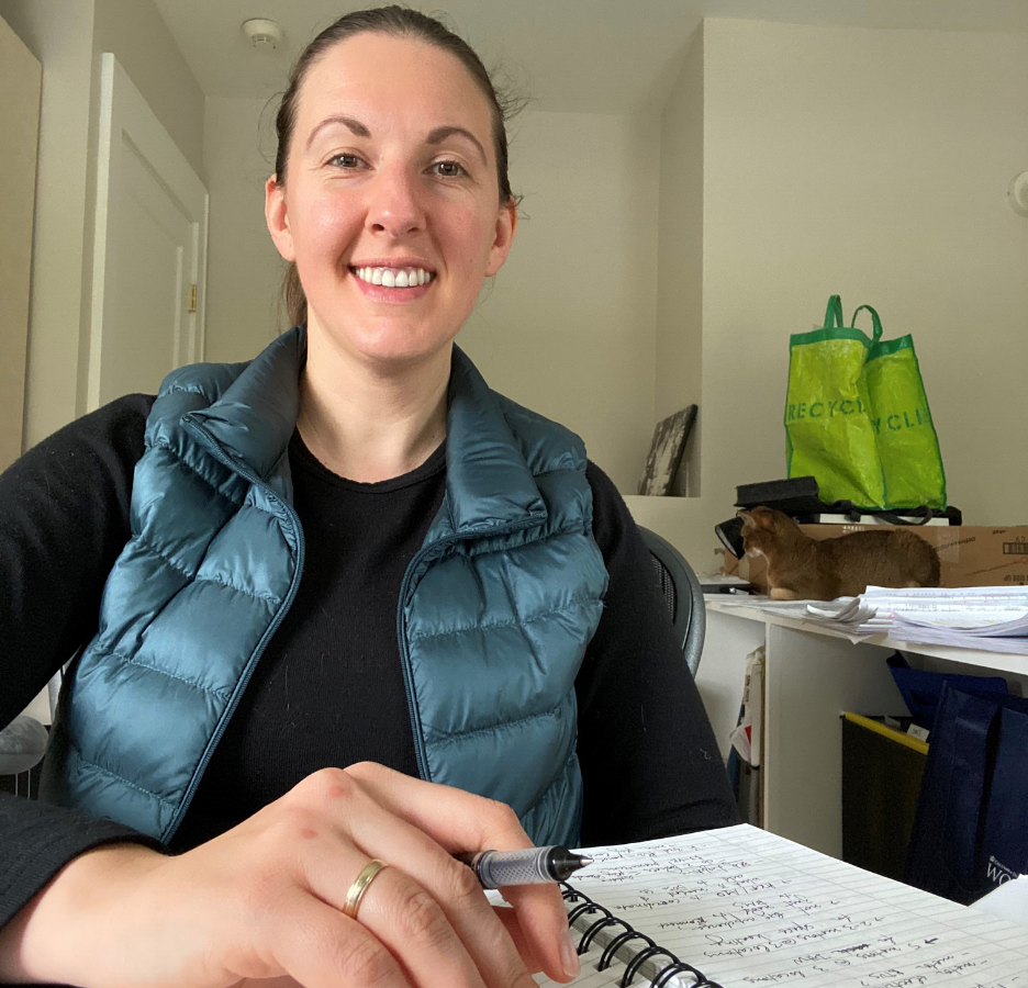 A woman wearing a puffy vest sits in front of a notebook