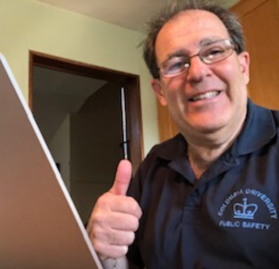 A man with glasses facing a laptop makes a thumbs-up sign.