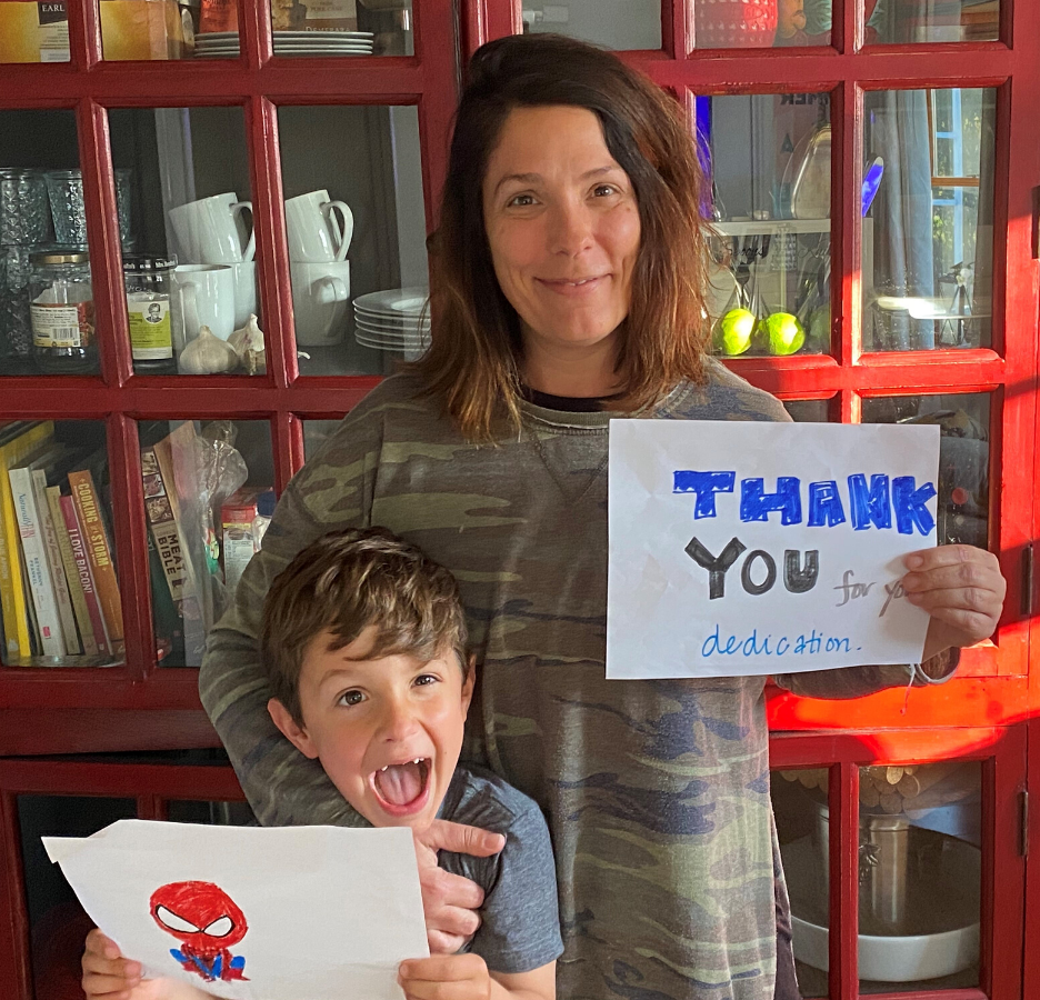 A young boy holding a handmade picture of Spiderman stands next to a woman holding a handmade thank you sign.