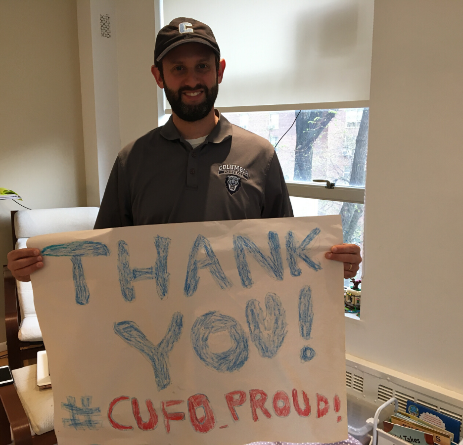 A man wearing a baseball cap holds a poster that says, "Thank you / #CUFO Proud"