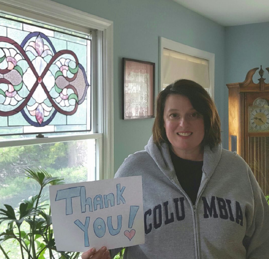 A woman wearing a grey Columbia-branded jacket holds a handmade thank you sign