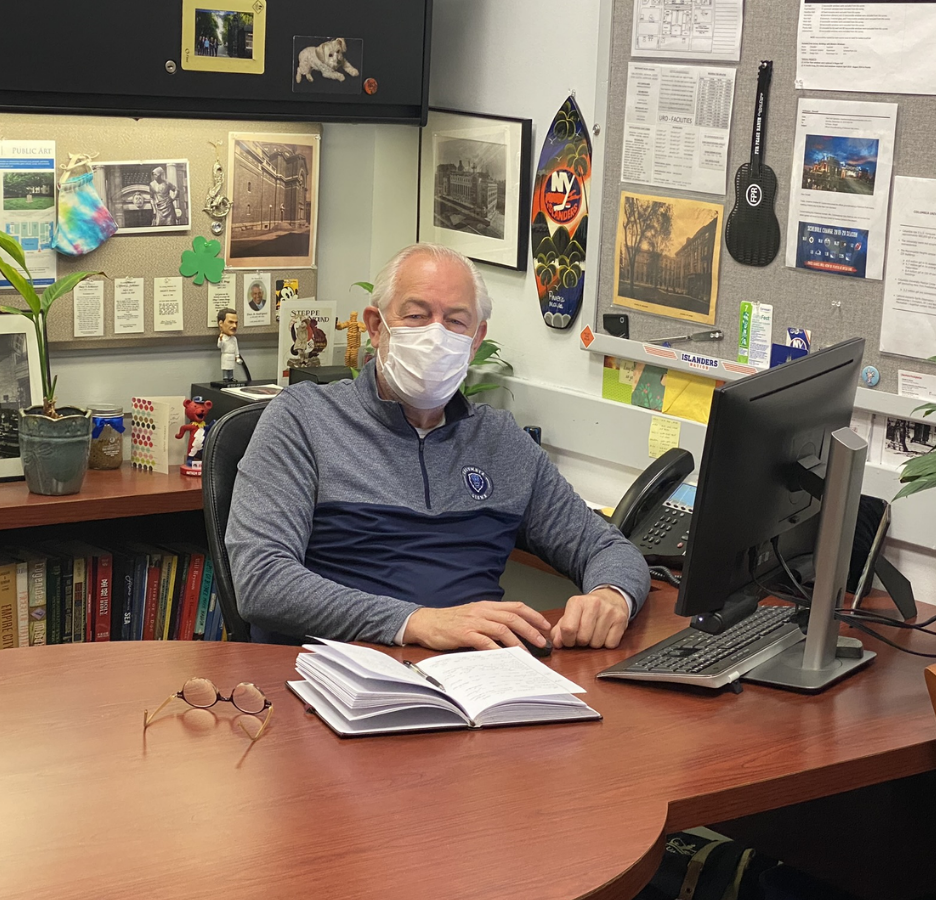 A man wearing a mask sits at a desk in an office