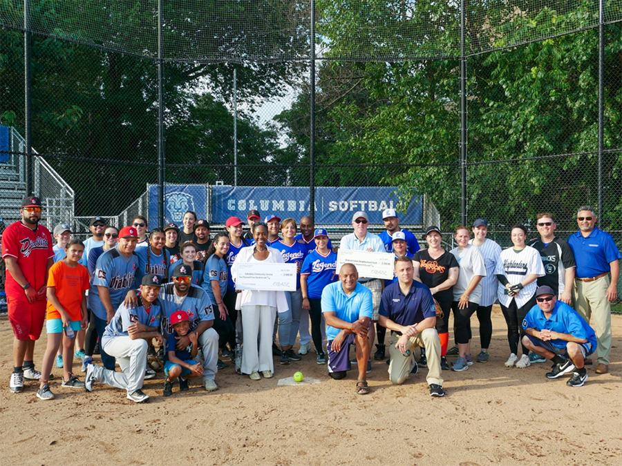 Several members of the Columbia staff softball league pose with Christa Hill of Columbia Community Service and Ross Frommer of the Medical Center Neighborhood Fund, both holding the checks presented for charity. Photo: Caroline Moore/Campus Services