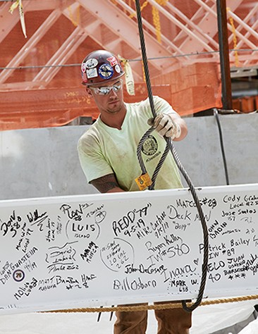 Construction worker secures steel cable around beam.