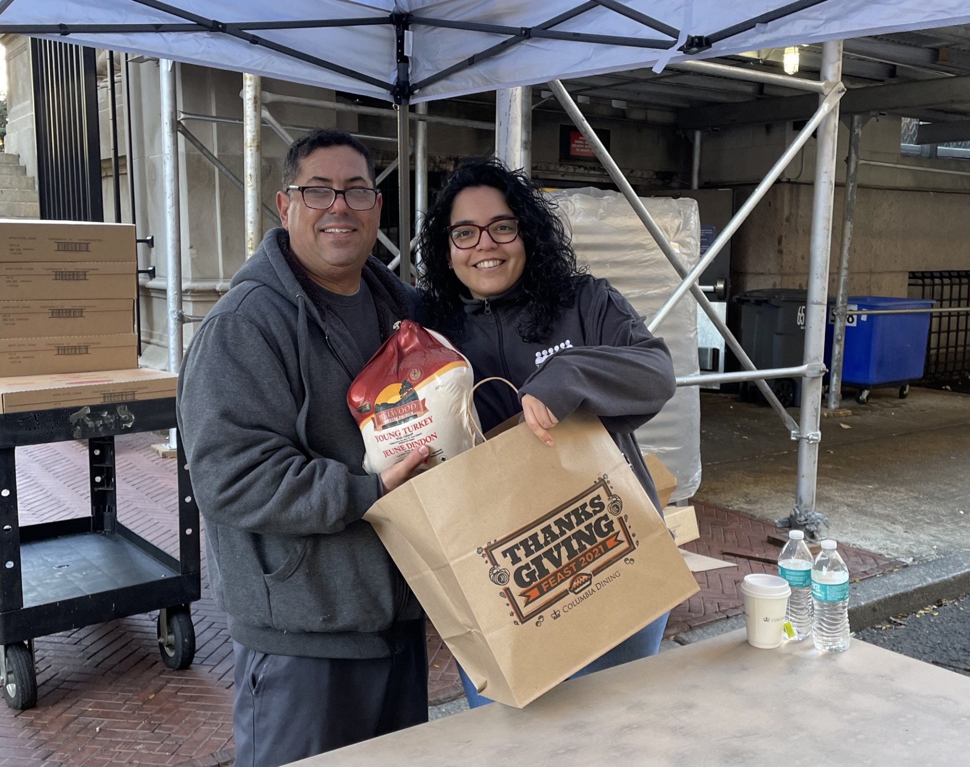 Chef Mike and Daphne Mendez from Columba Dining facilitate CUFO Thanksgiving dish distribution to employees. A man and a woman holding a turkey and bag that says: “Thanksgiving”