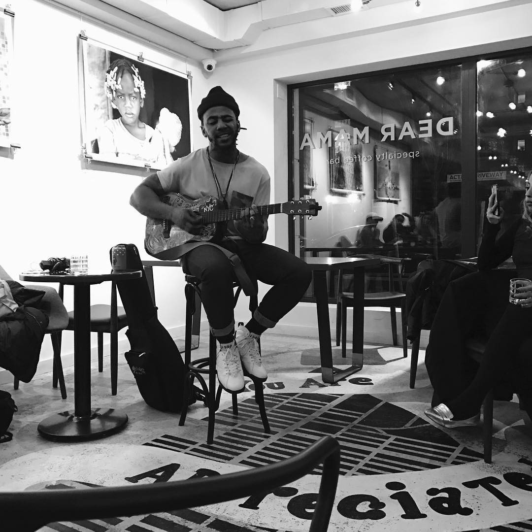 A musician sitting on a stool singing and playing guitar