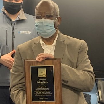 Patrol Captain is Delano Steele celebrates 14 years of perfect attendance and retirement after 36 years on the team. male wearing a light brown suit jacket and a face mask posing for a photo with plaque
