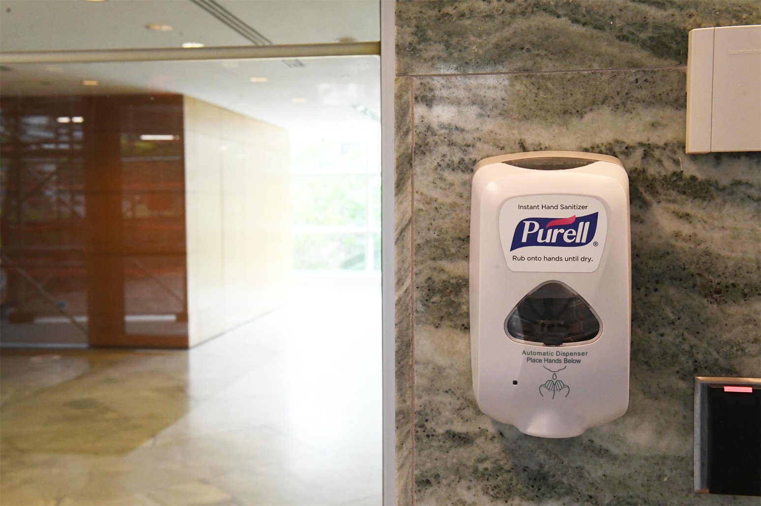 A Purell hand sanitizer dispenser installed on a granite wall