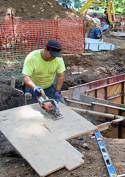 Worker using a power saw to cut a sheet of wood along the Math Walkway