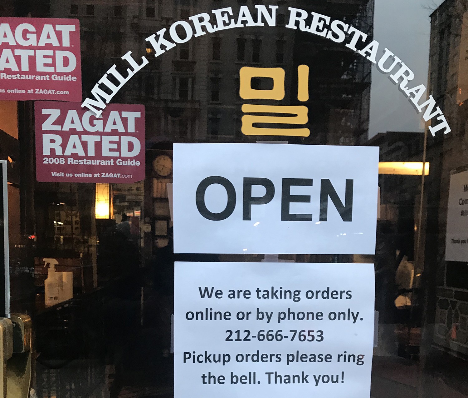 A sign stating that Mill Korean Restaurant is open for pickup and delivery orders.