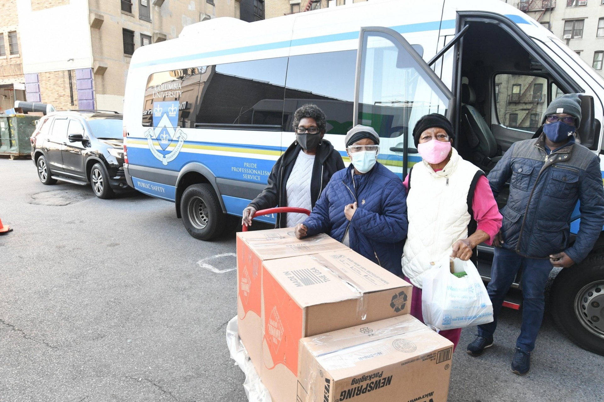 Facilities and Operations staff members safely deliver pre-Thanksgiving meals to local senior citizens. Photo Credit: Eileen Barroso Three women with face masks and one man with face mask accepting delivery box of food.